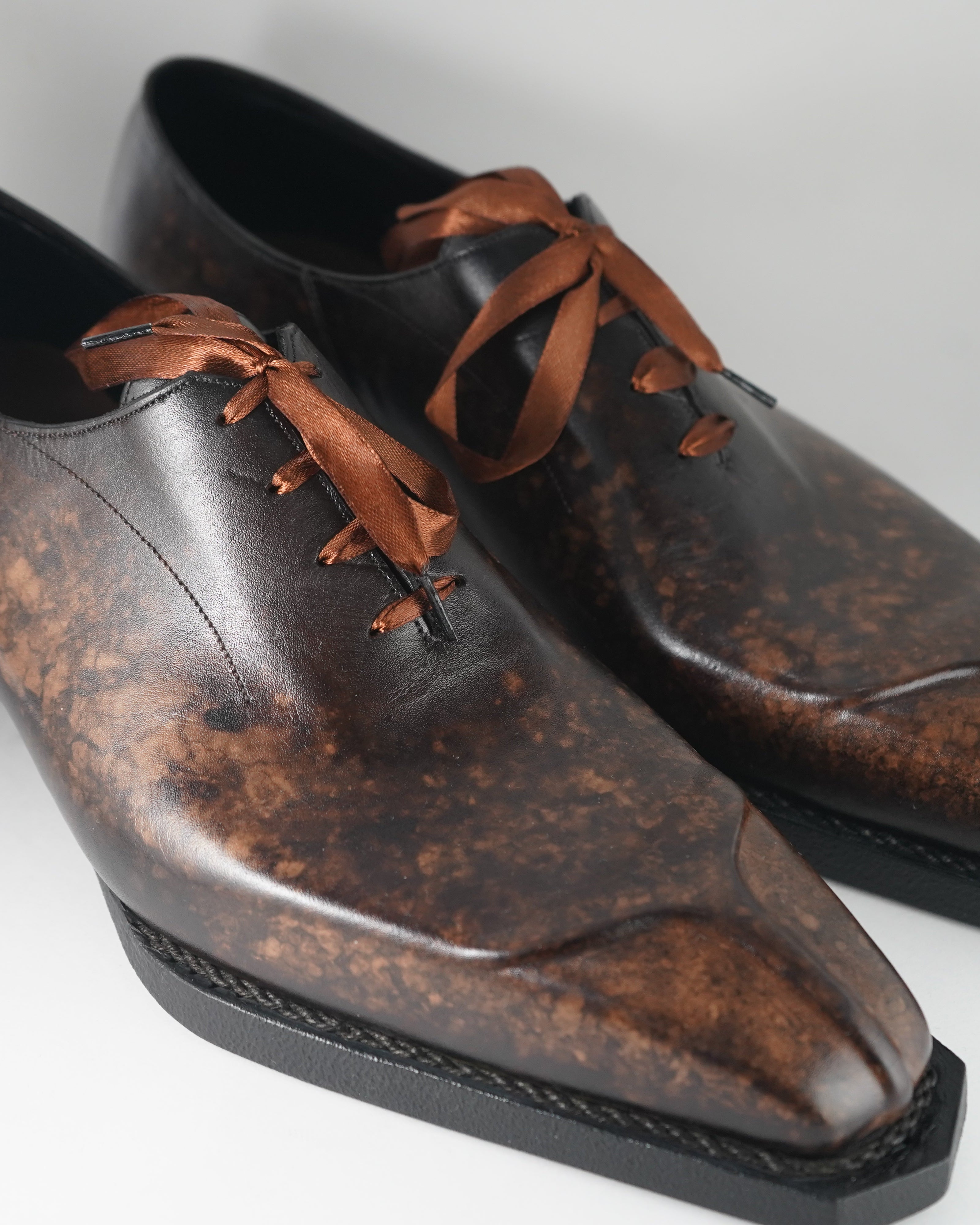 Brown leather dress shoes with brown laces on a white background.